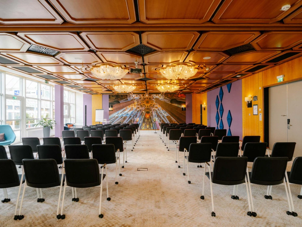 Stilvoller Konferenzraum mit moderner Bestuhlung, Holzdecke mit Kronleuchtern, großen Fenstern und einer kreativen Wandgestaltung, ideal für Business-Events.