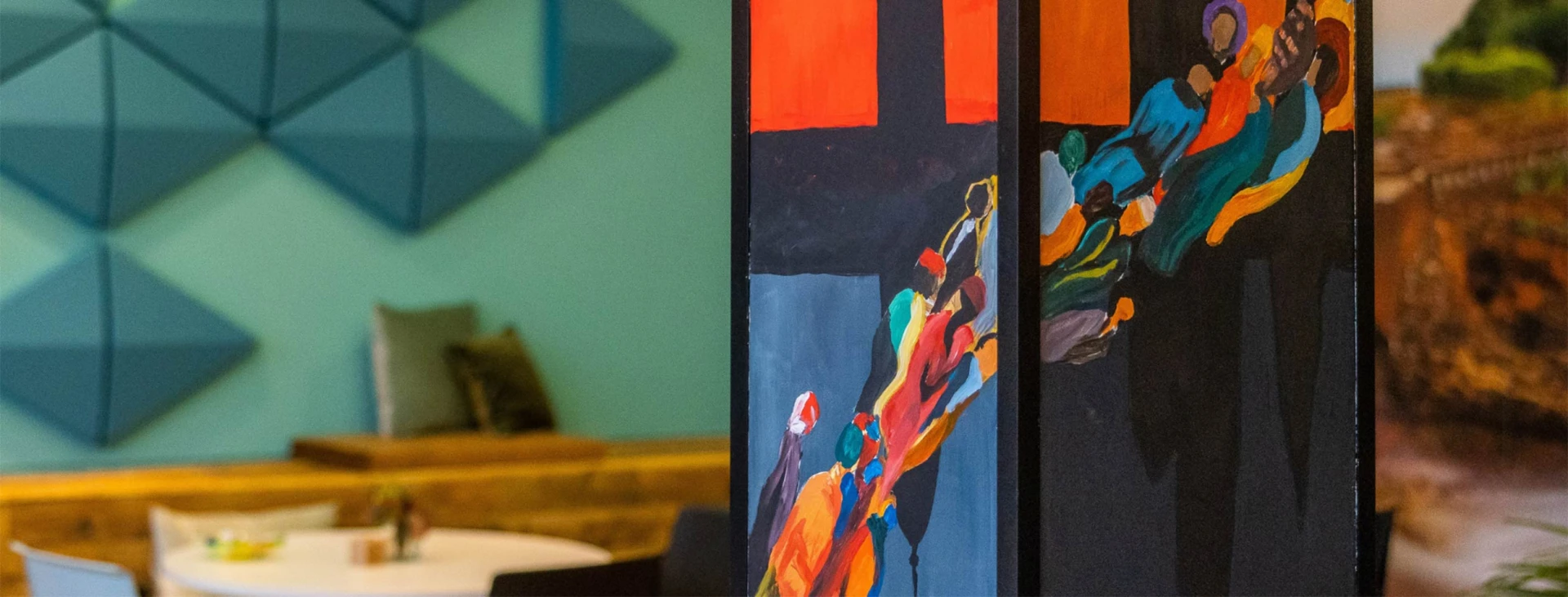 Detailaufnahme einer bunt bemalten Säule mit abstrakten Figuren in einem modernen Café. Im Hintergrund Sitzgelegenheiten, Holz- und Wanddekorationen.