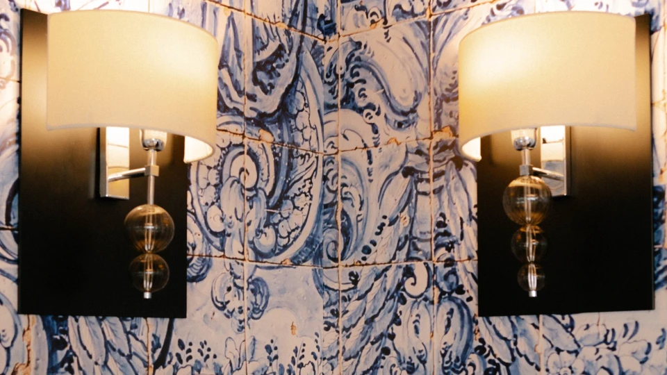 Zwei Wandlampen mit Glasdetails an einer blau-weißen Kachelwand mit Engeln und floralen Verzierungen