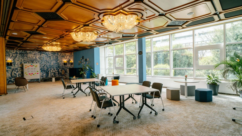 Großer Konferenzraum mit flexibler Bestuhlung, blauer Wand mit kunstvollen Fliesen und großen Fenstern mit Gartenblick