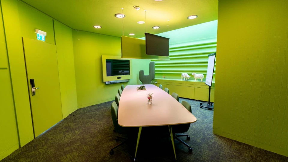 Modern gestalteter Besprechungsraum in Grün mit langem Tisch, Hängedeko, TV-Bildschirm und kreativen Wandstrukturen