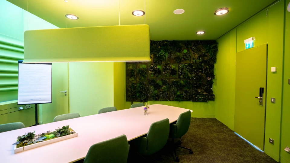 Moderner Konferenzraum mit grünen Wänden, großem Besprechungstisch, vertikaler Pflanzenwand und hängendem Akustikelement