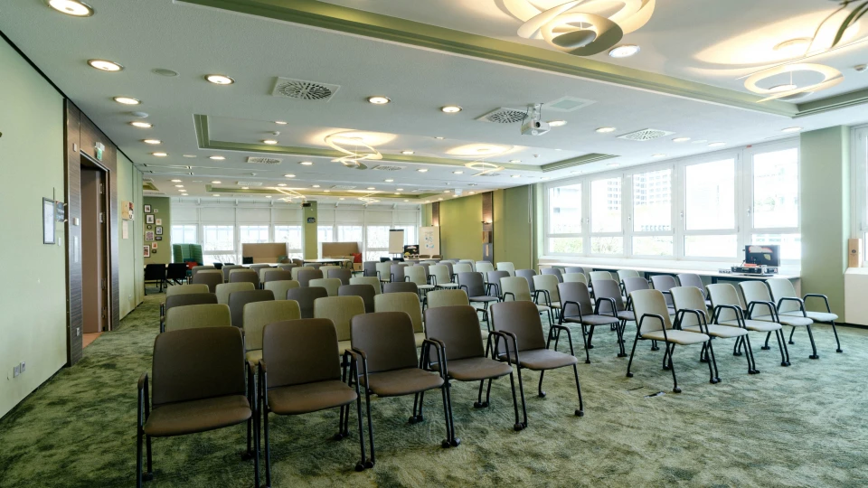 Moderner Konferenzraum mit Reihenbestuhlung, grüner Teppichgestaltung, stilvollen Deckenleuchten und großer Fensterfront