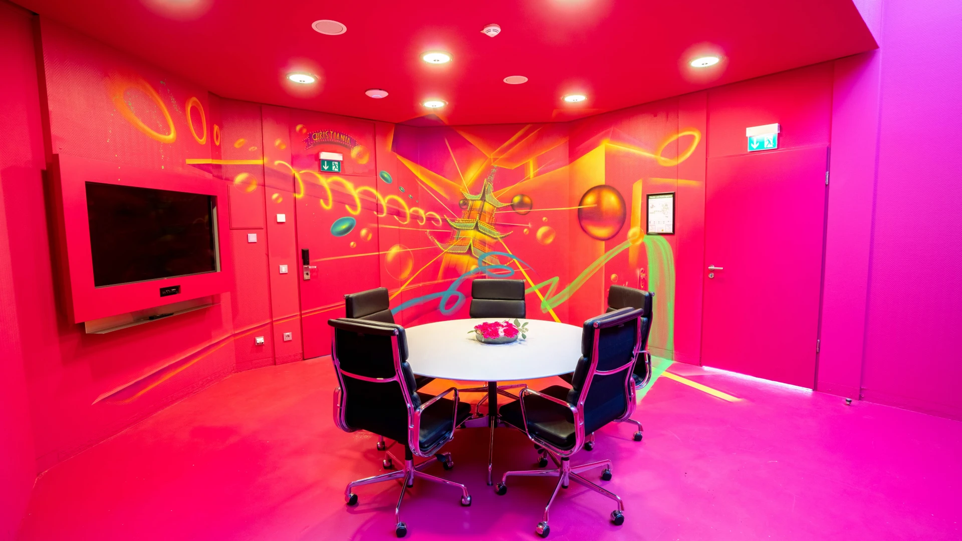 Futuristisch gestalteter Meetingraum mit intensiver pinker Farbgebung, runden Konferenztisch und Graffiti-Wandkunst mit leuchtenden Farben und abstrakten Formen