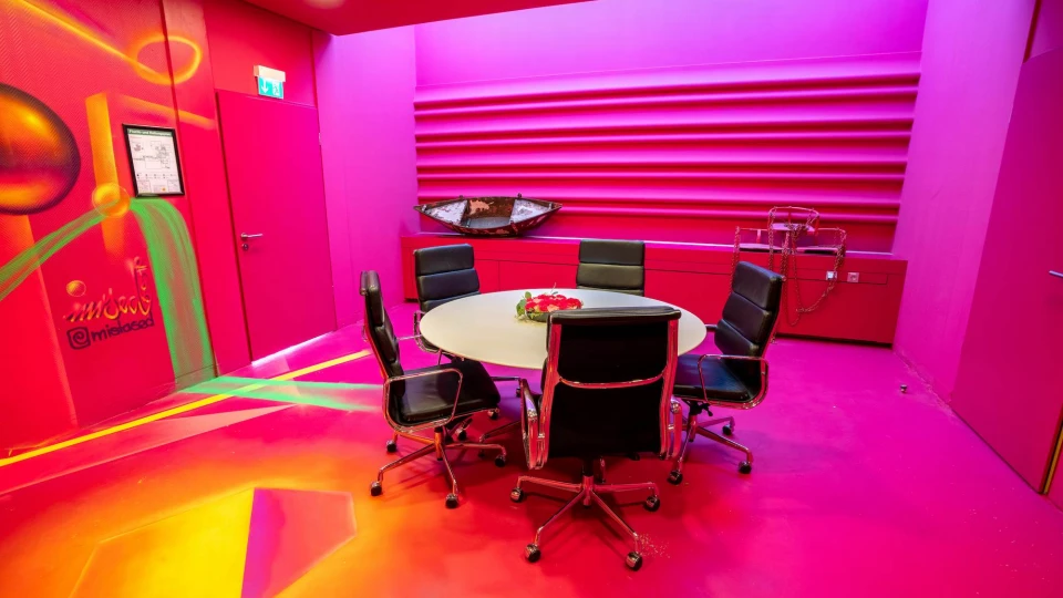 Moderner Meetingraum mit intensiver pinker Farbgestaltung, rundem Konferenztisch mit schwarzen Lederstühlen und auffälliger Graffiti-Wand mit leuchtenden Farben