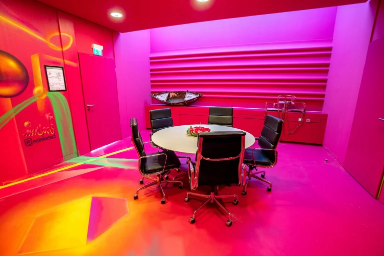 Moderner Meetingraum mit intensiver pinker Farbgestaltung, rundem Konferenztisch mit schwarzen Lederstühlen und auffälliger Graffiti-Wand mit leuchtenden Farben