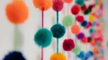 Bunte Pompon-Girlanden hängen an einer Wand und sorgen mit kräftigen Farben für eine fröhliche Raumgestaltung