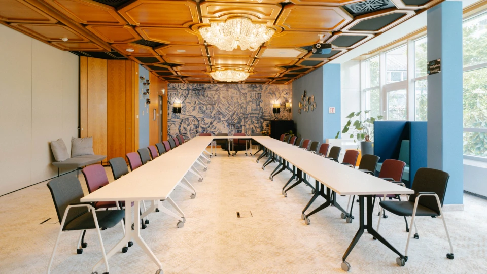 Eleganter Konferenzraum mit U-förmiger Tischanordnung, goldener Decke und kunstvollen Wandfliesen