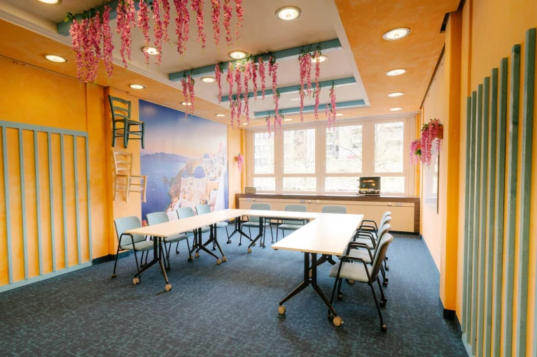 Meetingraum mit mediterranem Flair, blauen Akzenten, Wandkunst und hängenden Blumen für eine inspirierende Atmosphäre