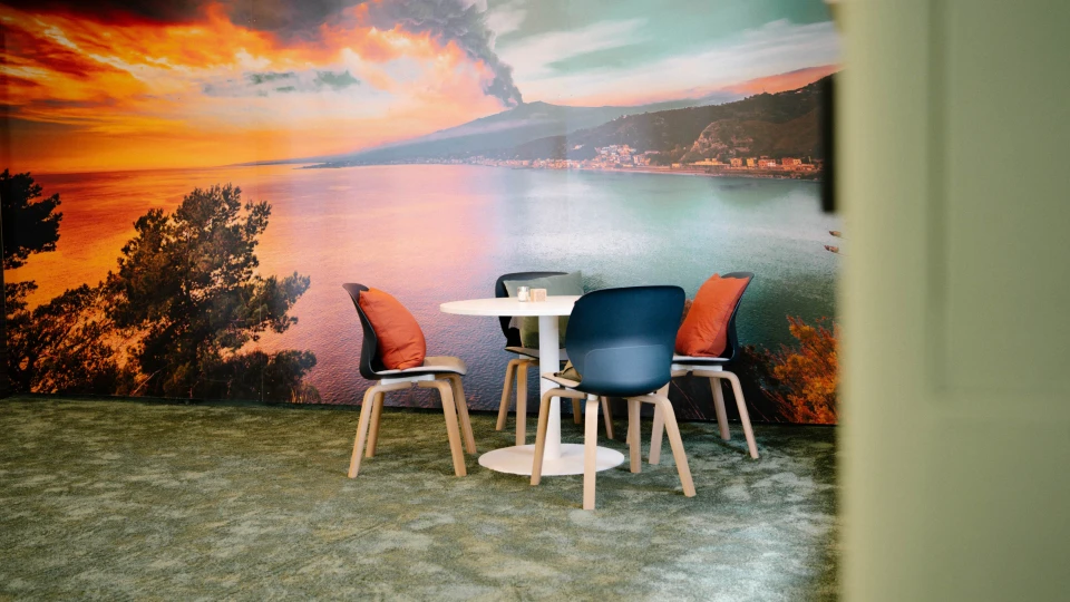 Runder Tisch mit Stühlen vor Sizilien-Fotowand und gemütlichem Ambiente im Smartvillage München