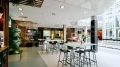 Heller Cafébereich mit Stehtischen, Hockern und Blick auf Besprechungsräume und Schaukelbank
