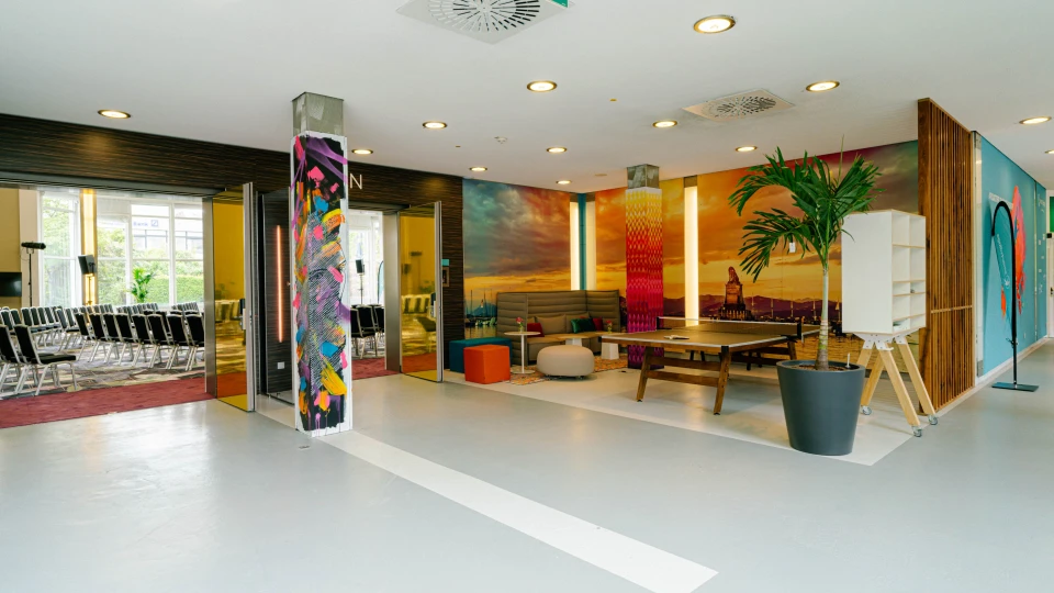 Farbenfrohe Lounge mit Sitzlandschaft, bunten Wandmotiven und Eingang zu Konferenzräumen