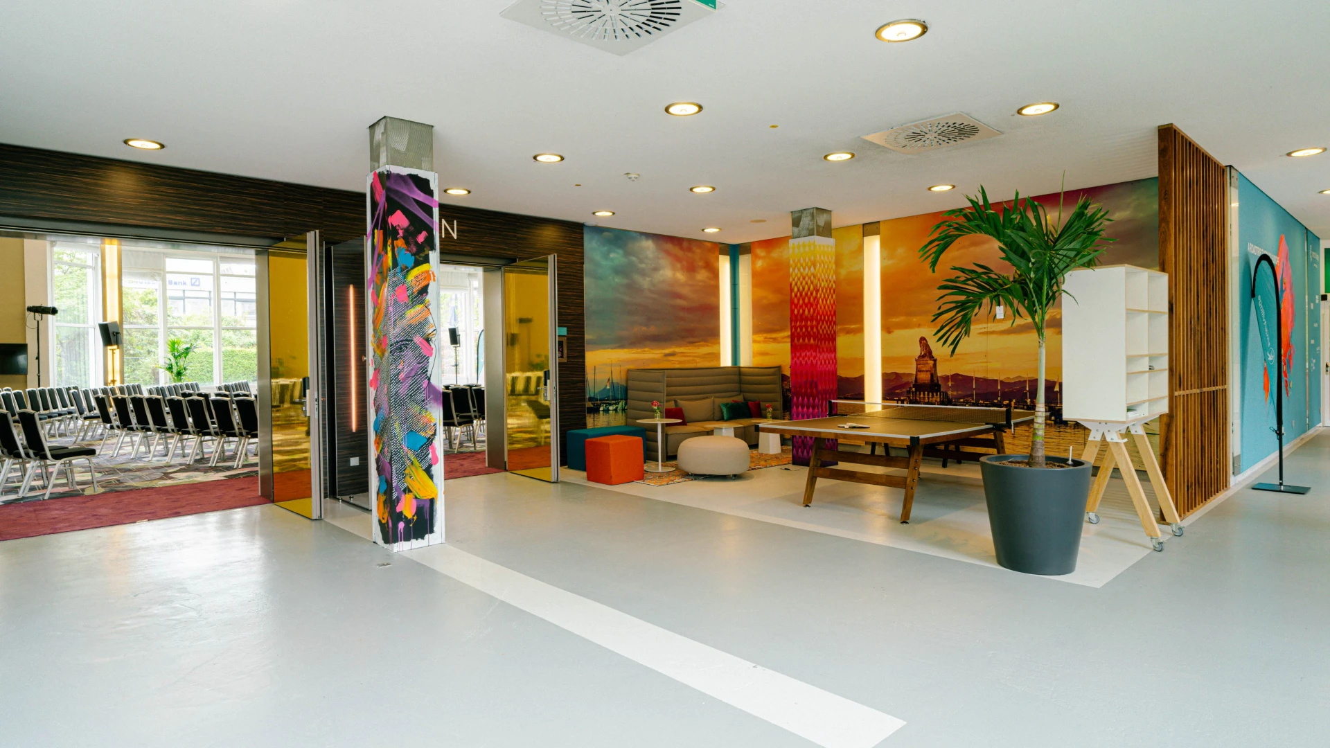 Farbenfrohe Lounge mit Sitzlandschaft, bunten Wandmotiven und Eingang zu Konferenzräumen