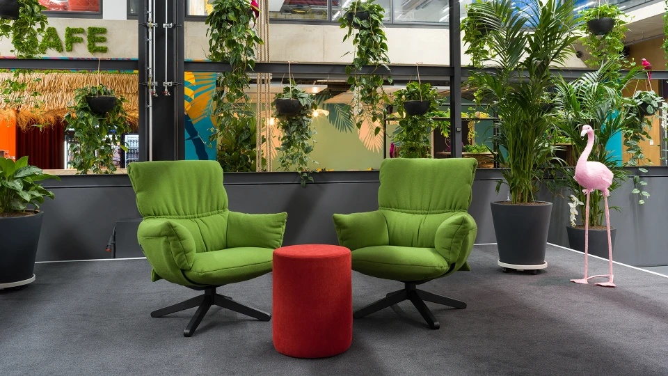 Zwei grüne Designersessel mit rotem Hocker vor tropischen Pflanzen im smartvillage Coworking Space